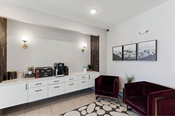 A living room with a white wall, a black and white rug, and two red chairs.
